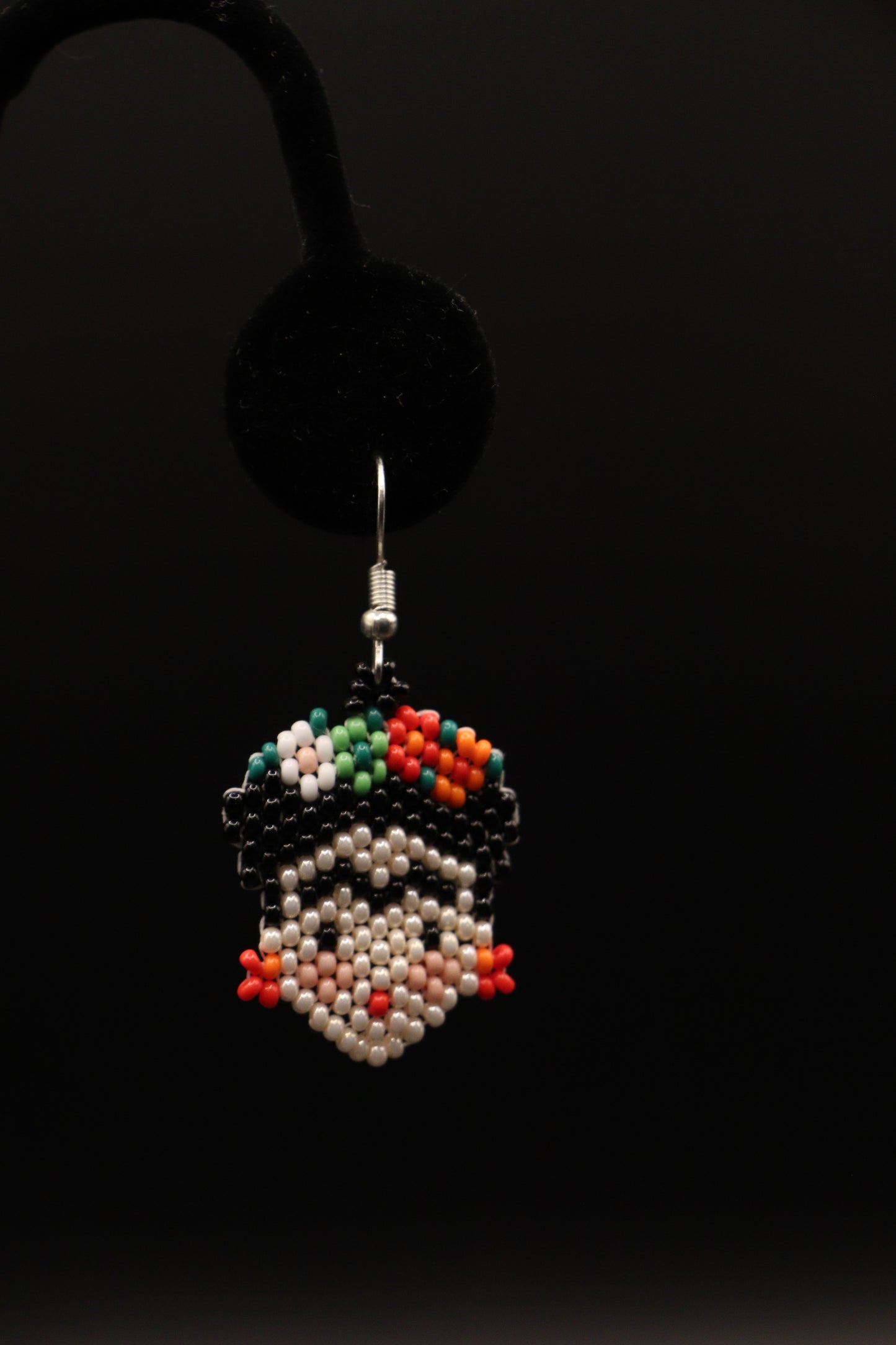 Colorful handcrafted Frida inspired seed bead earrings hanging on a display with a black background.