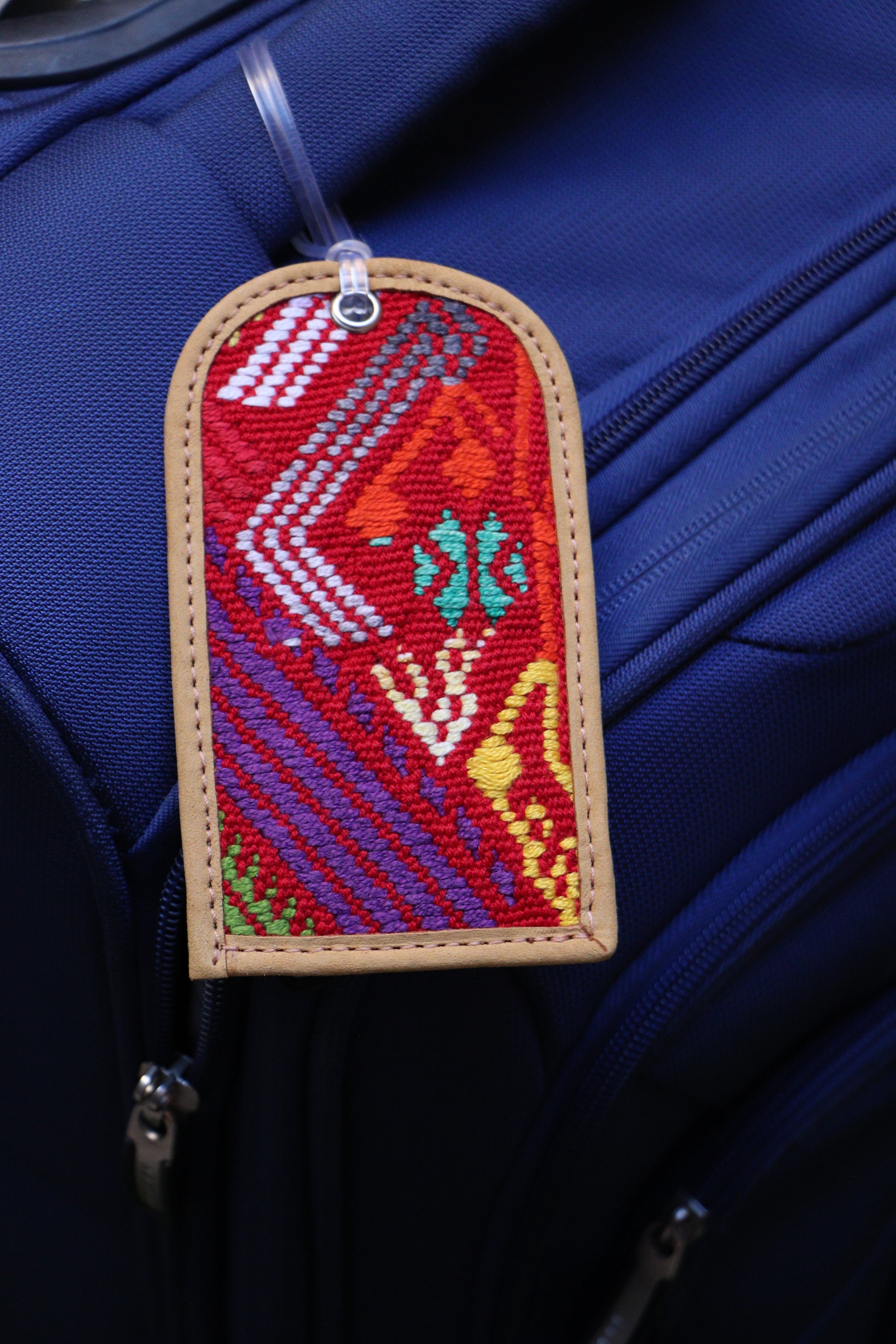 A handwoven luggage tag featuring geometric patterns in red, blue, and green, attached to a blue suitcase.