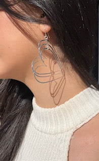 A close-up image of a woman wearing silver stacked heart earrings.