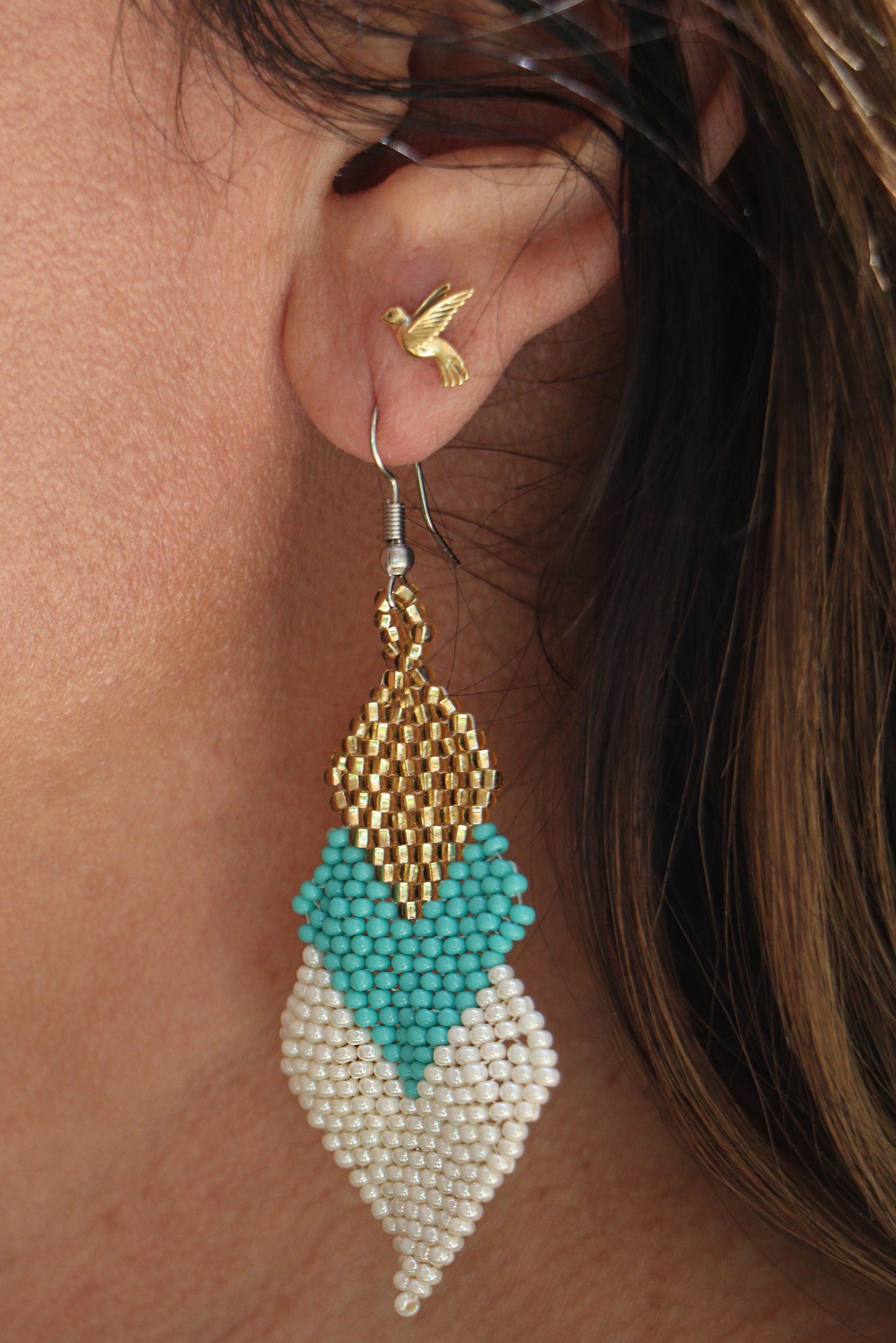 Close-up of gold, turquoise, and white beaded earrings.