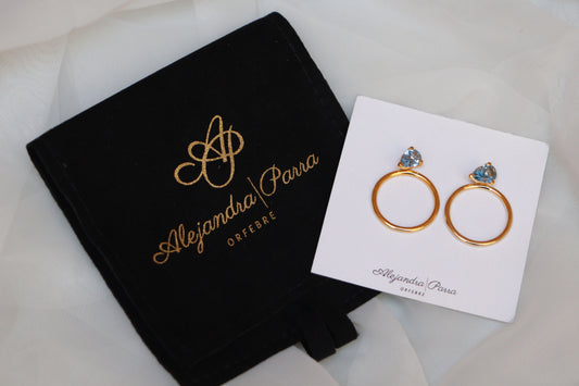 Aquamarine gold hoop earrings with blue gemstone displayed on Alejandra Parra jewelry card