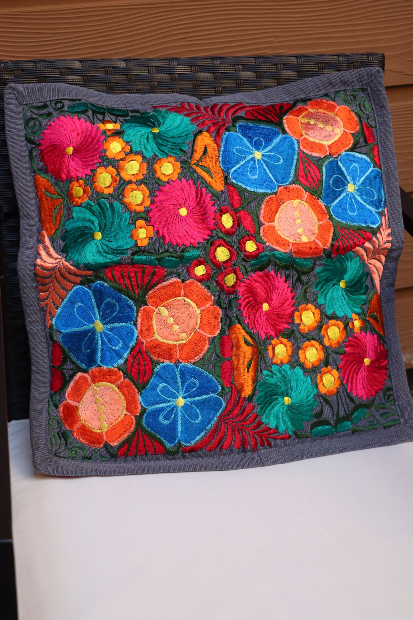 A multicolored handmade embroidered pillowcase with a floral pattern displayed on patio furniture.