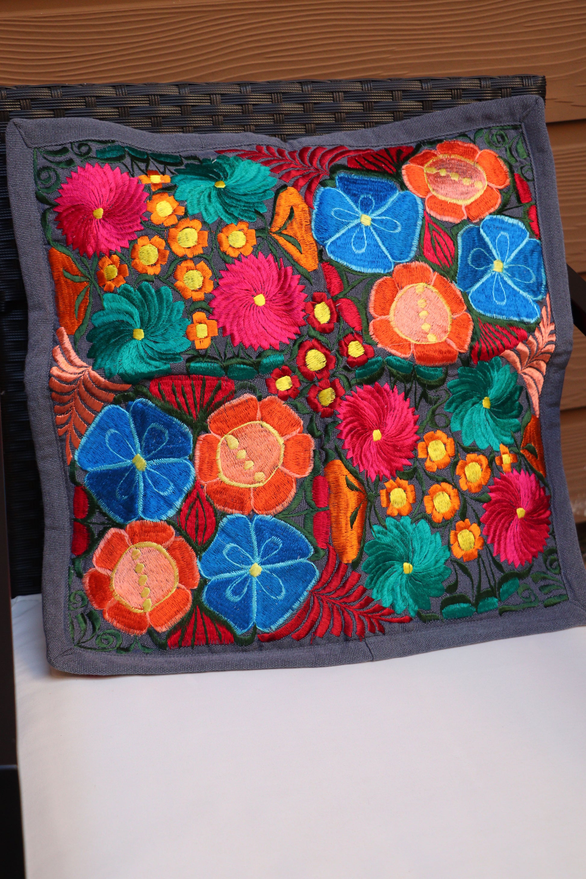 A multicolored handmade embroidered pillowcase with a floral pattern displayed on patio furniture.