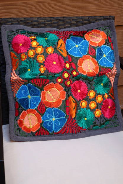 A multicolored handmade embroidered pillowcase with a floral pattern displayed on patio furniture.