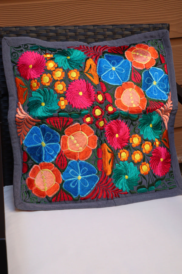 A multicolored handmade embroidered pillowcase with a floral pattern displayed on patio furniture.