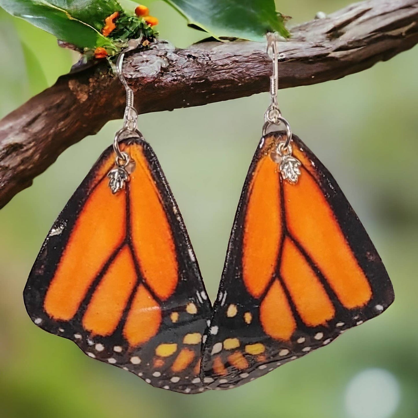 Handmade butterfly-wing shaped earrings hanging on a branch with green leaves.