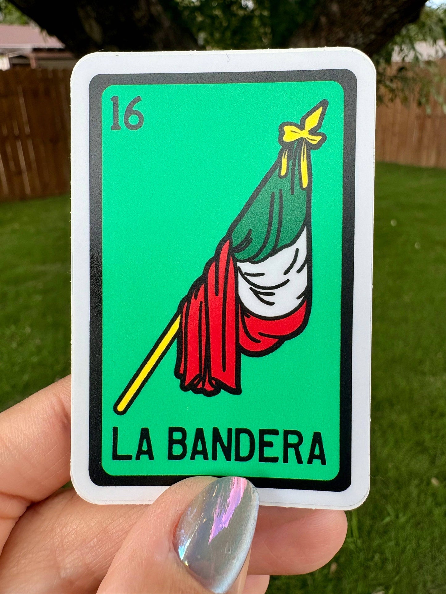 Vinyl sticker with 'La Bandera' loteria inspired design held by a hand outdoors.