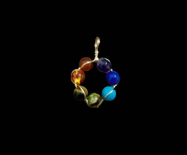 A multicolored round chakra pendant made of various stones, including red, orange, yellow, blue, purple, and green, set in a gold wire frame.