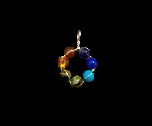 A multicolored round chakra pendant made of various stones, including red, orange, yellow, blue, purple, and green, set in a gold wire frame.